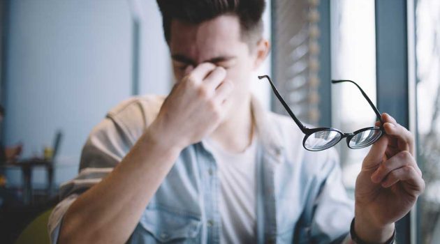 Young man with glasses rubbing his eyes