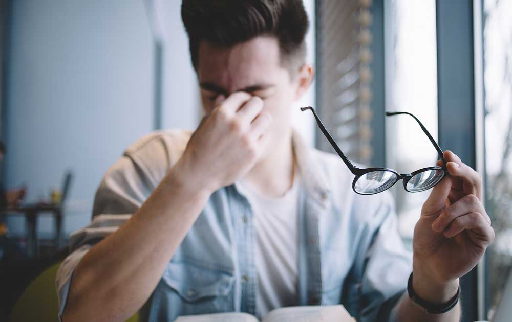 Young man with glasses rubbing his eyes